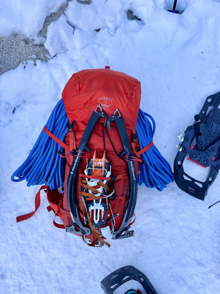 An orange backpack with a blue rope, ice axes, and crampons.