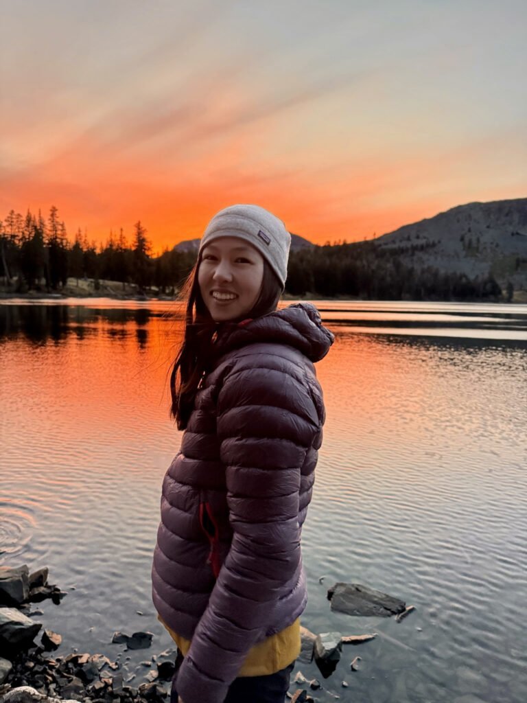 A woman standing against a sunset over an alpine lake