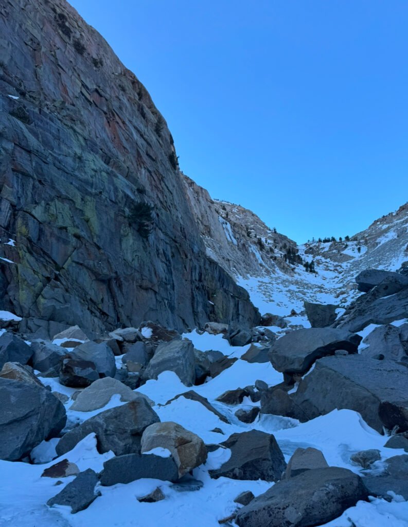 A snowy canyon with boulders and ice climbing routes in the far distance
