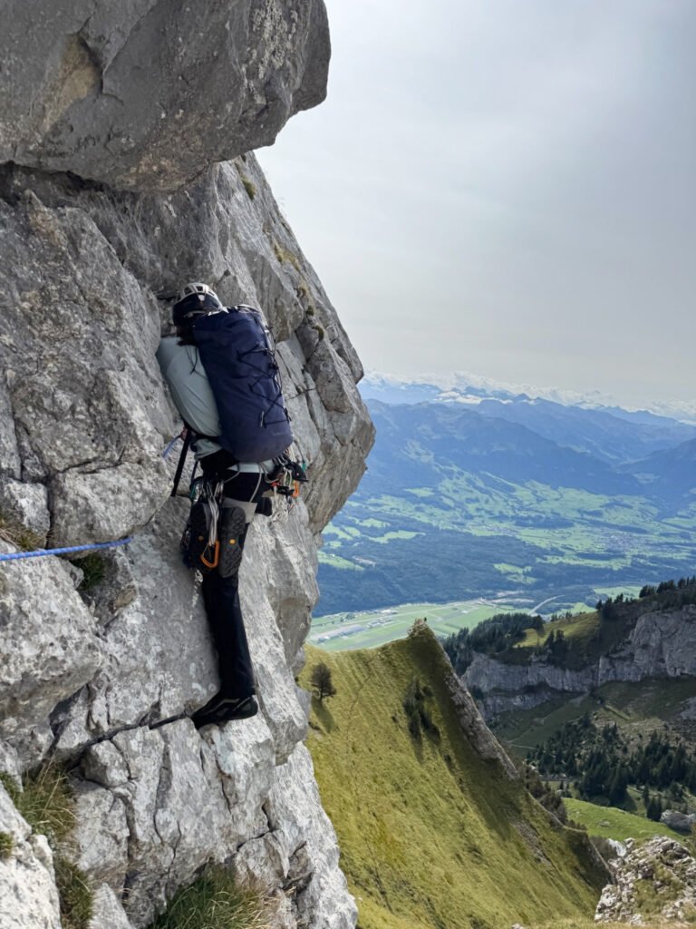A rock climber beginning a pitch, with mountains in the background.